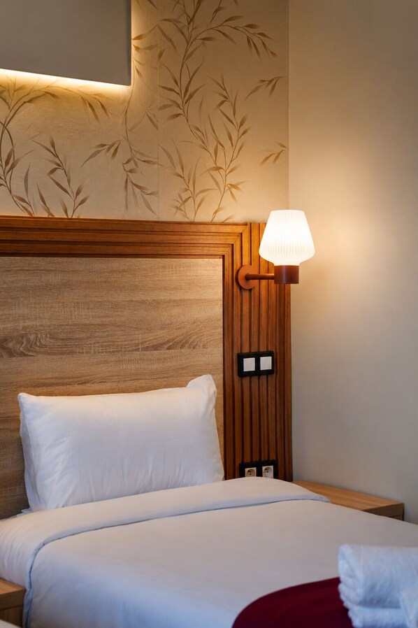 A hotel room with a wooden headboard, a bed with white bedding, a bedside lamp, and a wall with a bamboo leaf pattern.