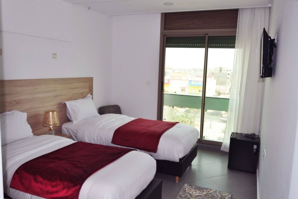 A hotel room with two beds, a TV, and a view of the city through a large window.