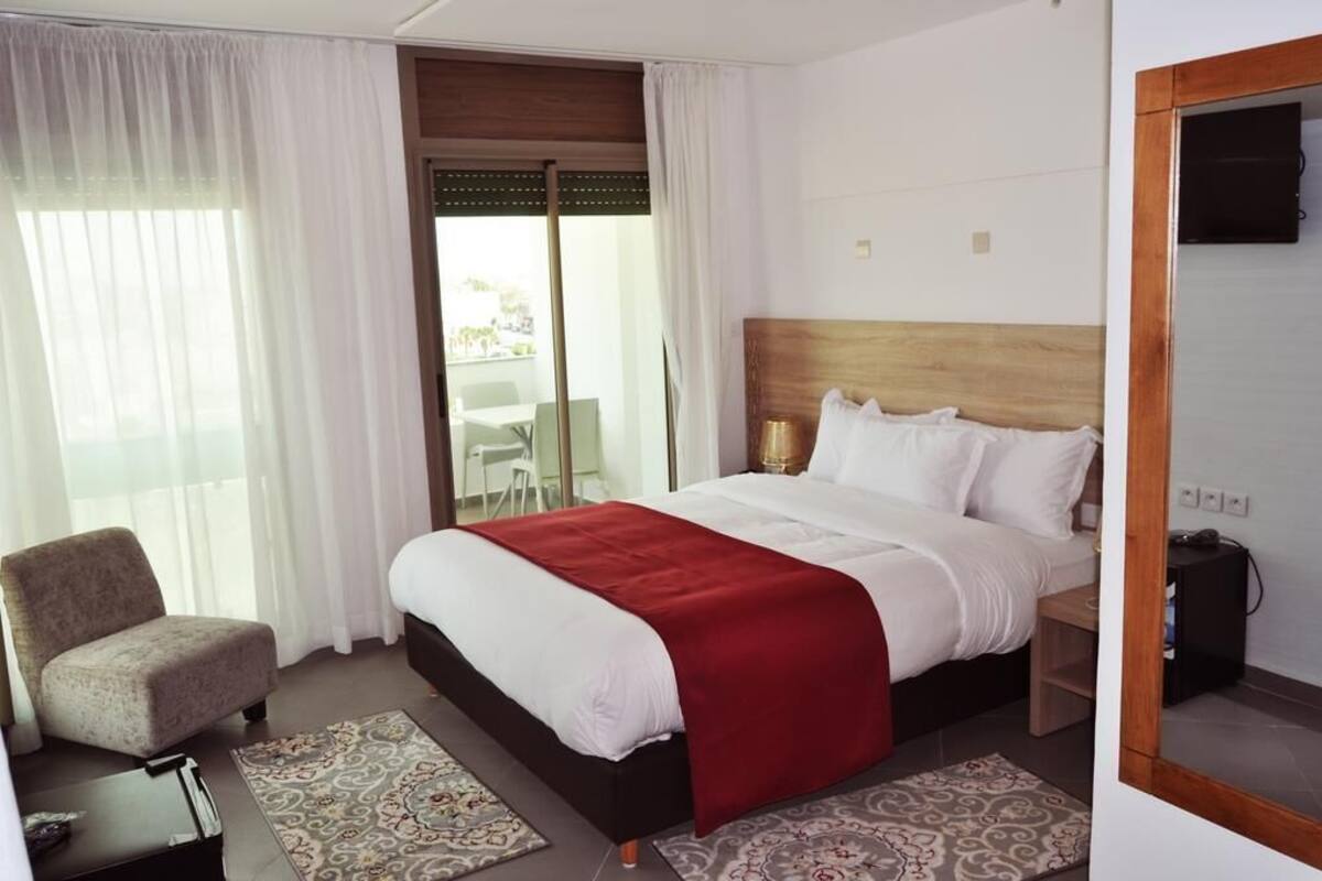 A hotel room with a bed, a chair, a TV, and a view of the outside.