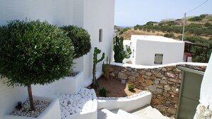 A white building with a stone wall and a small garden area with a tree and cacti. - Maistrali Studio - House Levante (Syros)