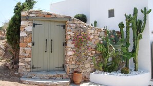 A stone-built entrance with a door, surrounded by cacti and a potted plant. - Maistrali Studio - House Levante (Syros)
