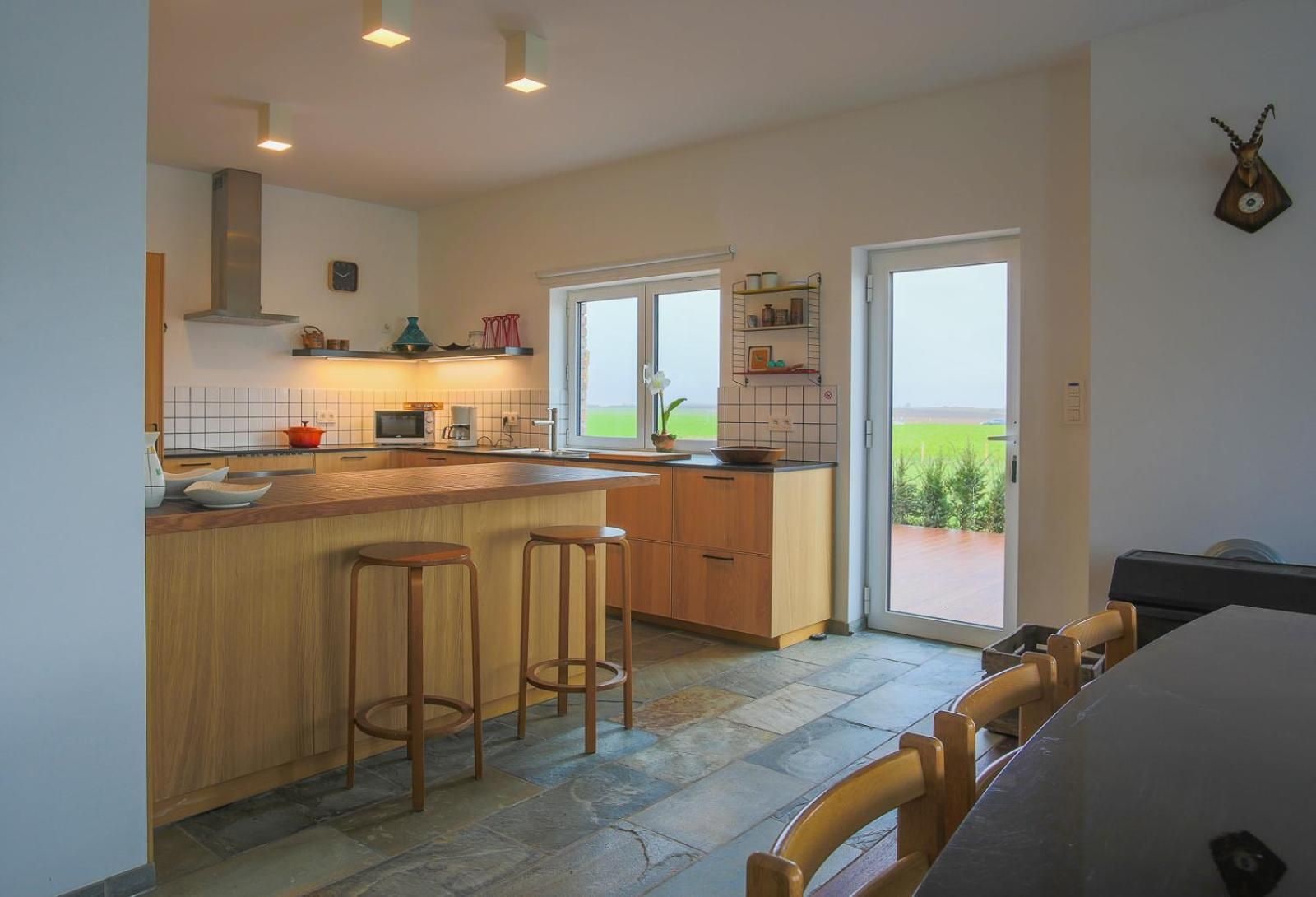 A modern kitchen with a central island, bar stools, and a view through a sliding glass door.