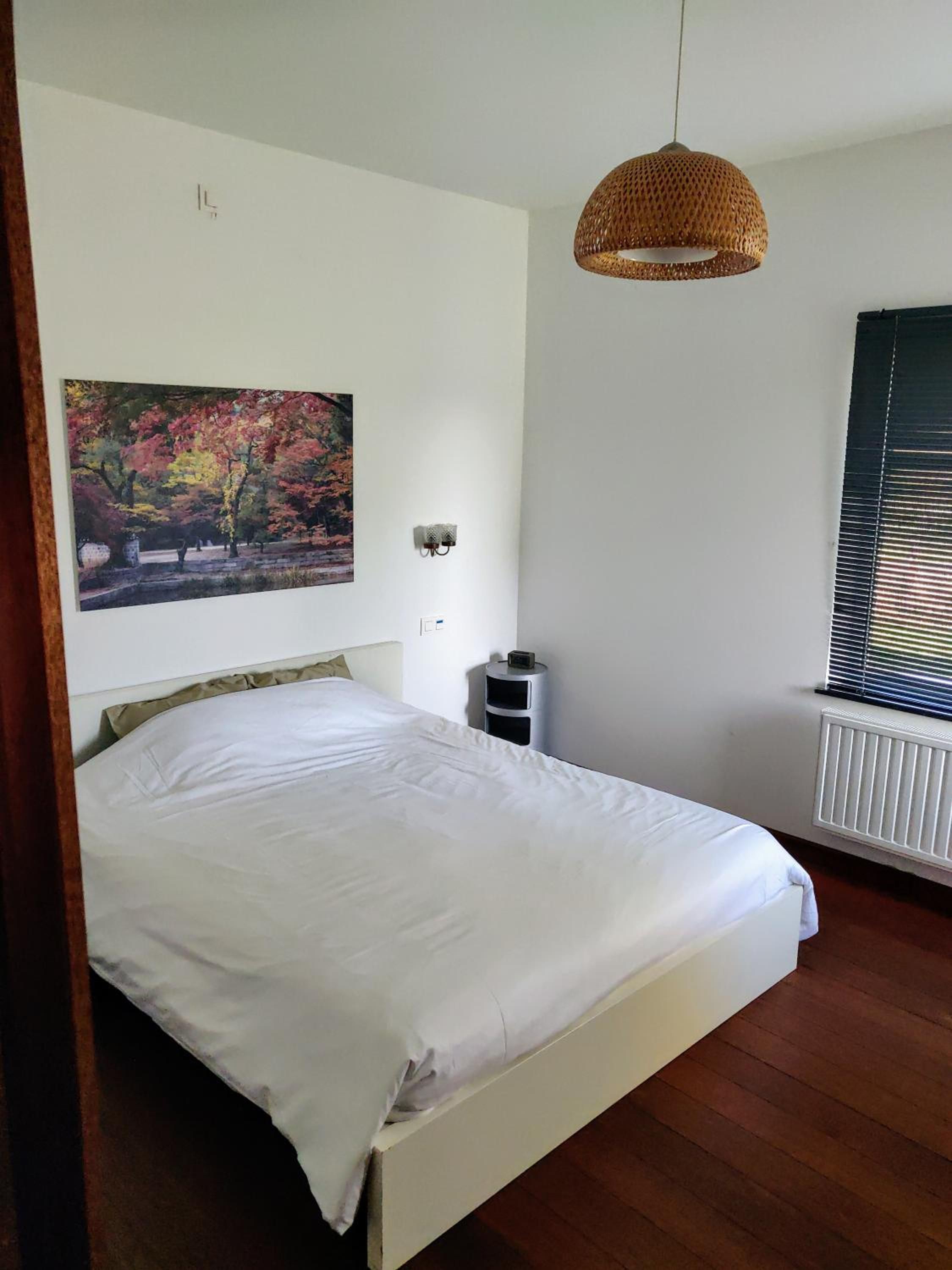 Une chambre à coucher comprenant un lit, une lampe fixée au mur, un radiateur et une fenêtre avec des stores.