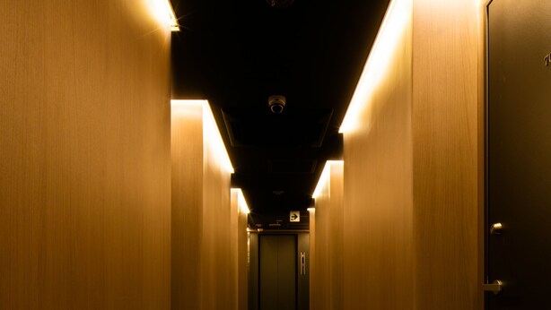 A narrow hallway with wooden walls and carpeted floor, leading to a door at the end. - Hills Hotel Gotanda (Tokyo)