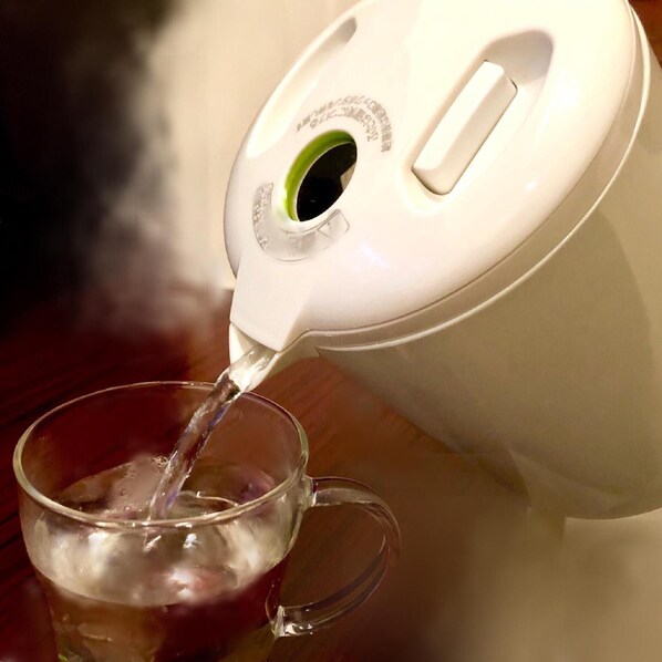 Une bouilloire électrique blanche verse de l’eau dans une tasse en verre transparent.