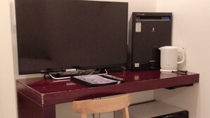 A compact workspace with a desk, chair, and a small refrigerator. - Hills Hotel Gotanda (Tokyo)