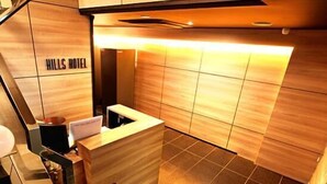 A reception area with a wooden reception desk, a small seating area, and a wall with the text "HILLS HOTEL". - Hills Hotel Gotanda (Tokyo)