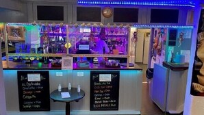 Eine Barbereich mit einer Neonreklame, einer Speisekarte und verschiedenen Ausstellungsstücken.