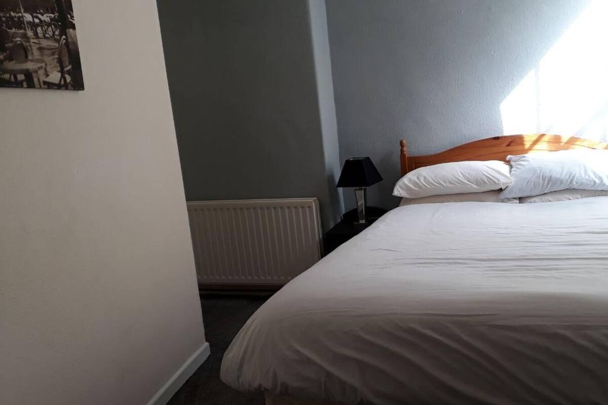 A bedroom with a bed, a nightstand, a lamp, and a radiator.