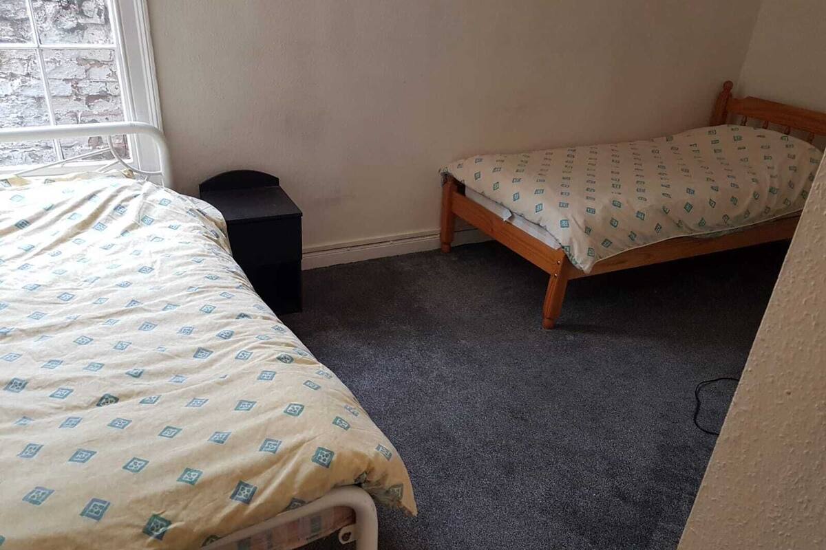 A bedroom with two beds, a window, and a black trash bin.