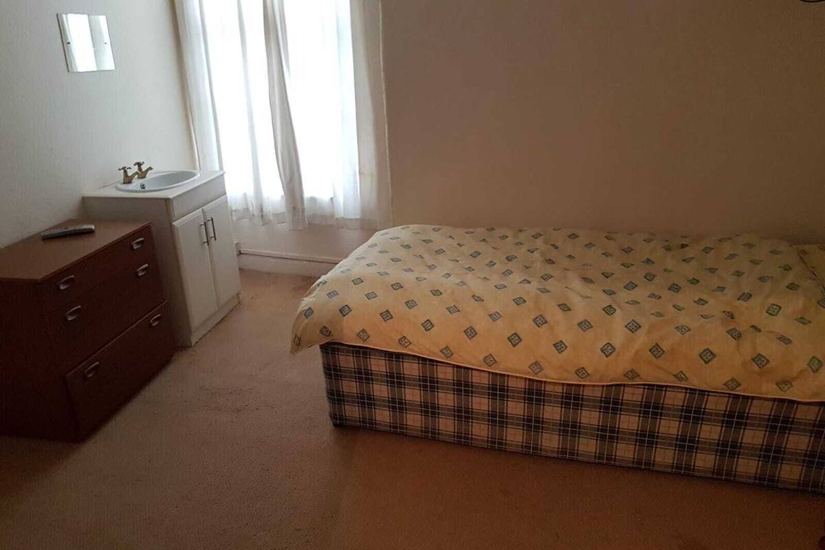 A bedroom with a bed, a dresser, a small white cabinet, and a window with curtains.