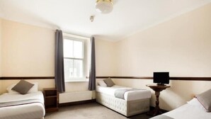 Ein Hotelzimmer mit zwei Einzelbetten, einem kleinen Tisch mit Fernseher und einem Fenster mit Vorhängen.