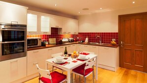 A modern kitchen with white cabinets, a double oven, a microwave, and a red-tiled backsplash. - Heads Nook Hall Cottage (Brampton)