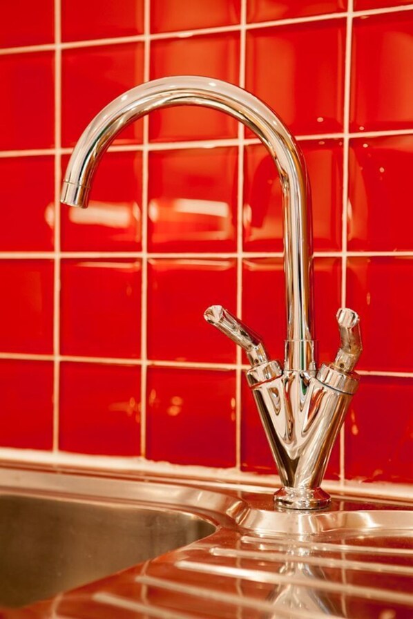 A chrome faucet with a unique design, set against a red tiled backsplash. - Heads Nook Hall Cottage (Brampton)