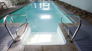 An indoor swimming pool with clear water, metal handrails, and a tiled floor.