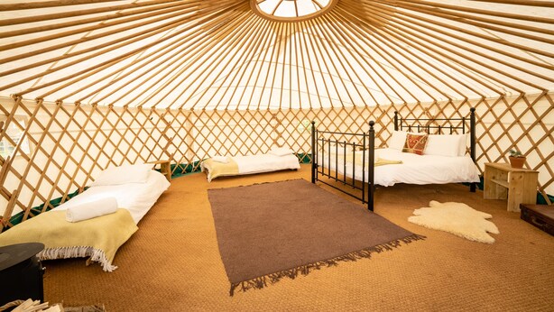 A yurt with two beds, a central rug, and a wooden floor.