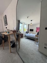Quarto de hotel moderno com cama, escrivaninha, cadeira, mesa pequena e espelho.