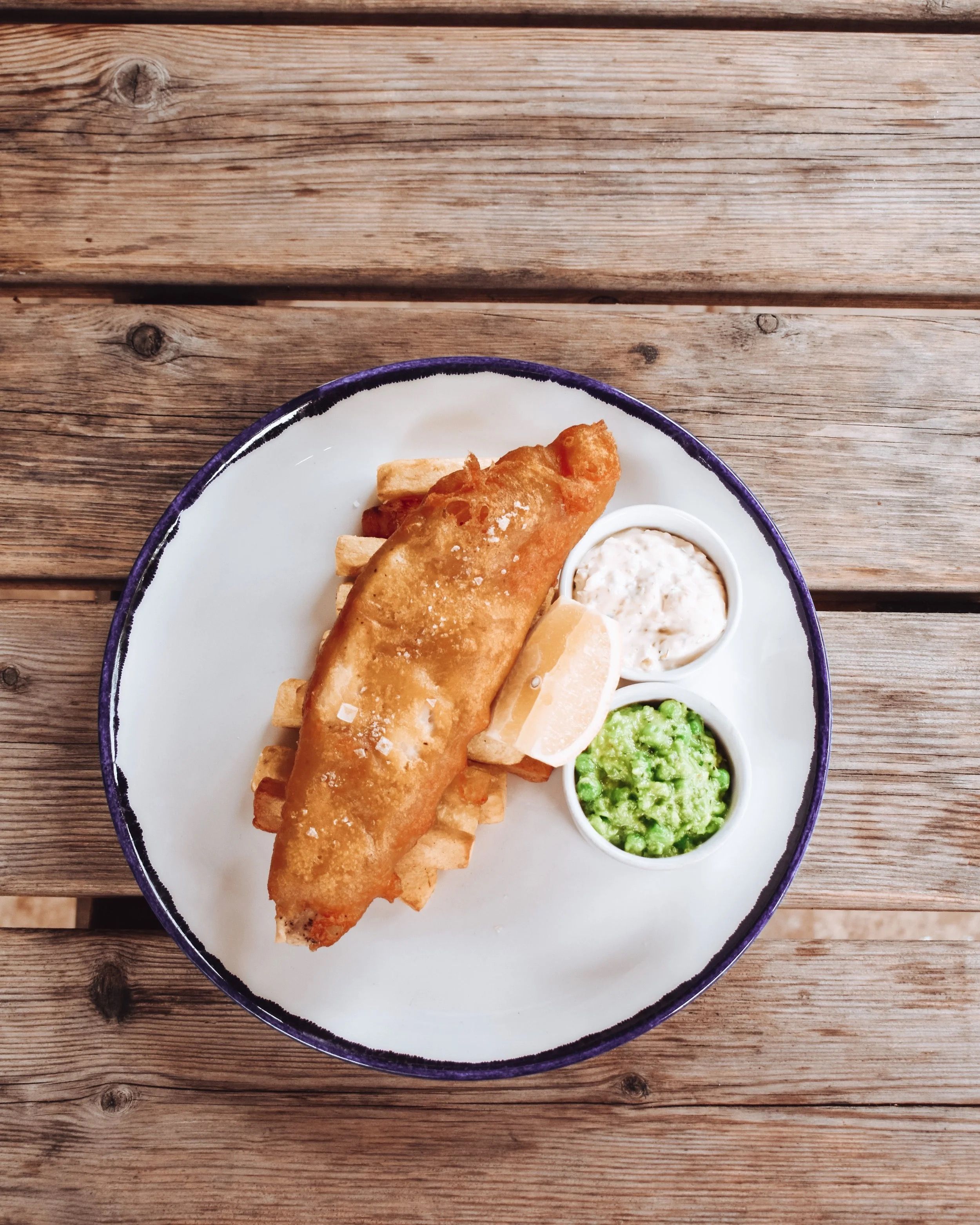 A plate with a fish fillet and two dipping sauces on a wooden table.