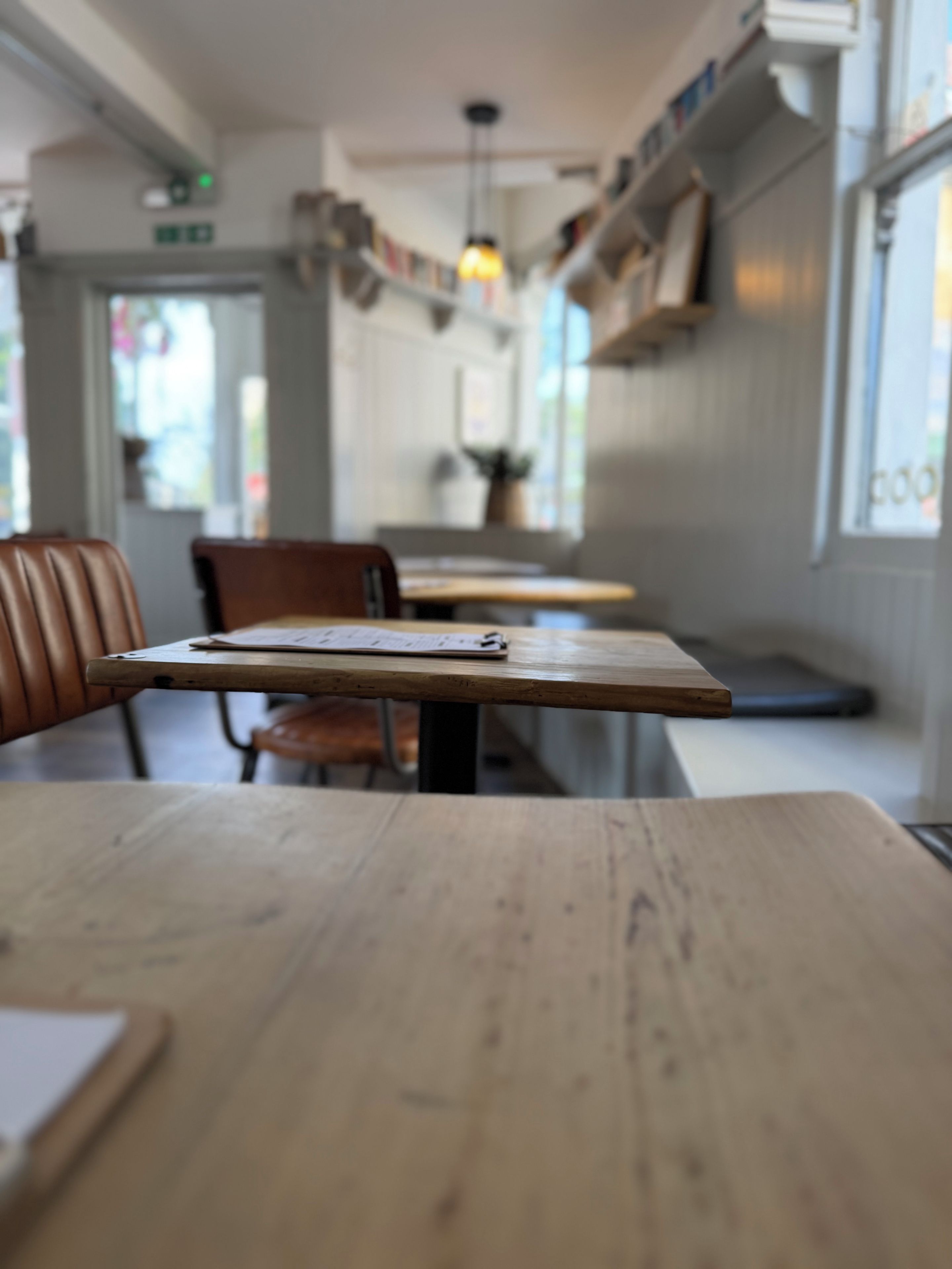 Een restaurant interieur met houten tafels en stoelen, een hanglamp en uitzicht door het raam.