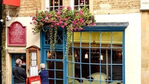 Un bâtiment à la façade bleue, orné d’une jardinière suspendue et d’une enseigne.