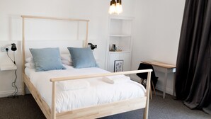 Une chambre moderne avec un lit en bois, deux oreillers, une table de chevet, un bureau et une étagère sur laquelle est posée une photo encadrée.