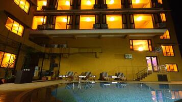 Una piscina con sillas de descanso y una escalera que conduce a un nivel superior con ventanas iluminadas.