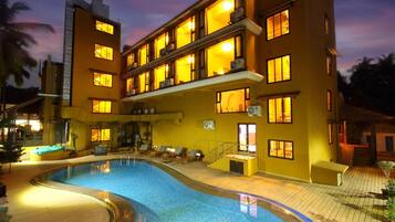 A hotel with a swimming pool, multiple balconies, and a sunset sky.