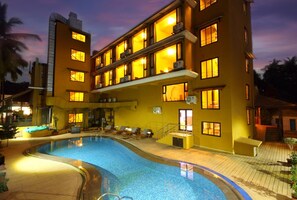 A hotel with a swimming pool, multiple balconies, and a sunset sky. - De Baga Deck Comforts (Calangute)