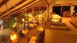 An indoor dining area with wooden tables and chairs, a sofa, and hanging lanterns. - De Baga Deck Comforts (Calangute)
