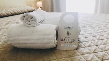 Una cama bien hecha con una toalla blanca doblada y un cartel que indica limpiar la habitación.