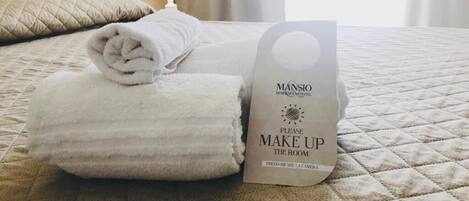 Una cama bien hecha con una toalla blanca doblada y un cartel que indica limpiar la habitación.