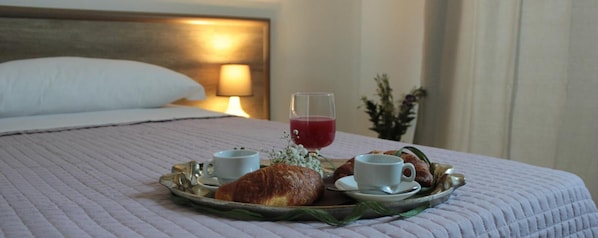 A neatly made bed with a tray of breakfast items including croissants, a glass of red juice, and two cups of coffee. - Mansio Residence Hotel (Elmas)