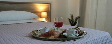 Una cama bien hecha con una bandeja de desayuno que incluye cruasanes, un vaso de jugo rojo y dos tazas de café.