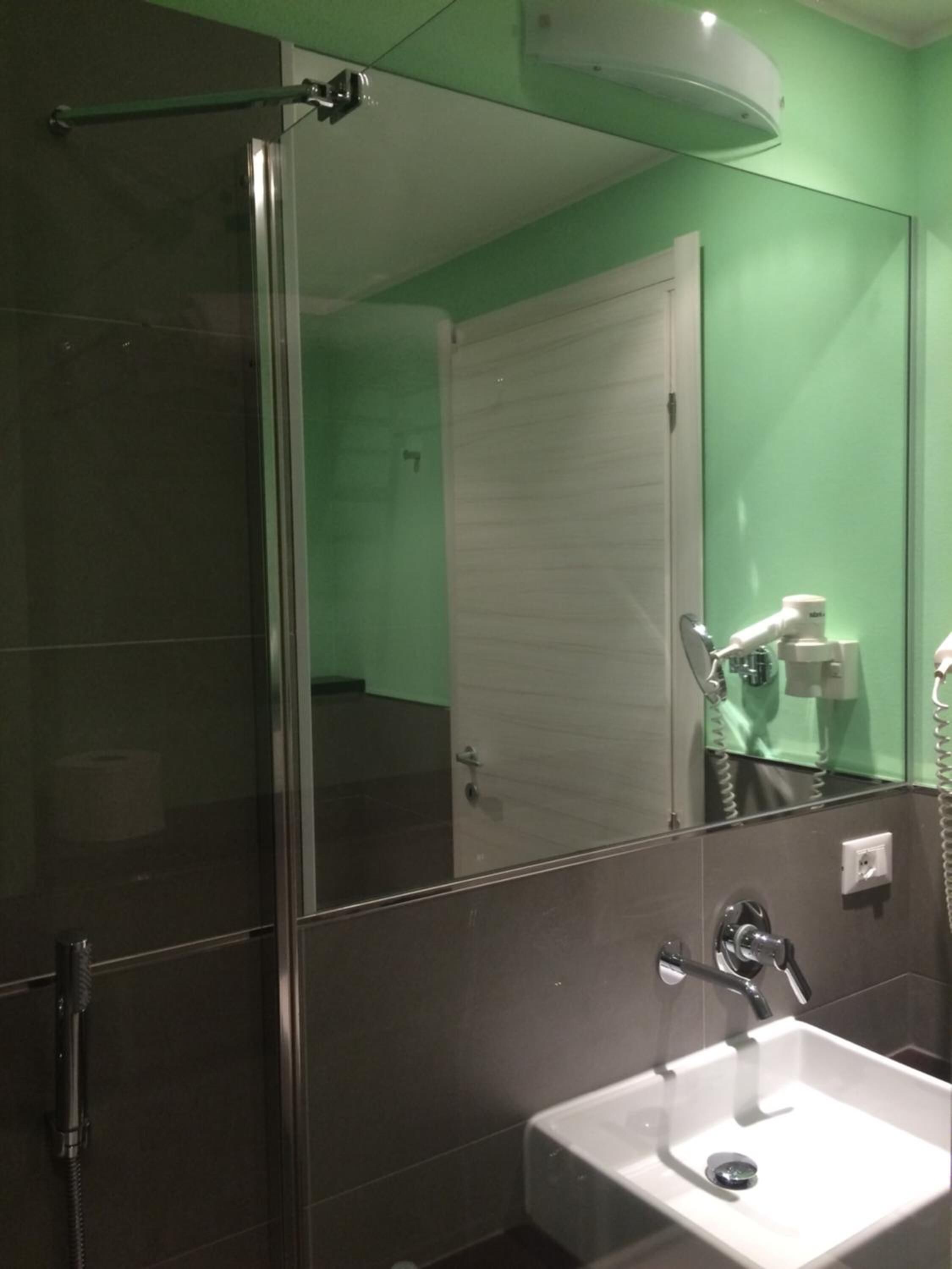 A bathroom with a glass shower enclosure, a sink, and a mirror reflecting a hairdryer and a door.