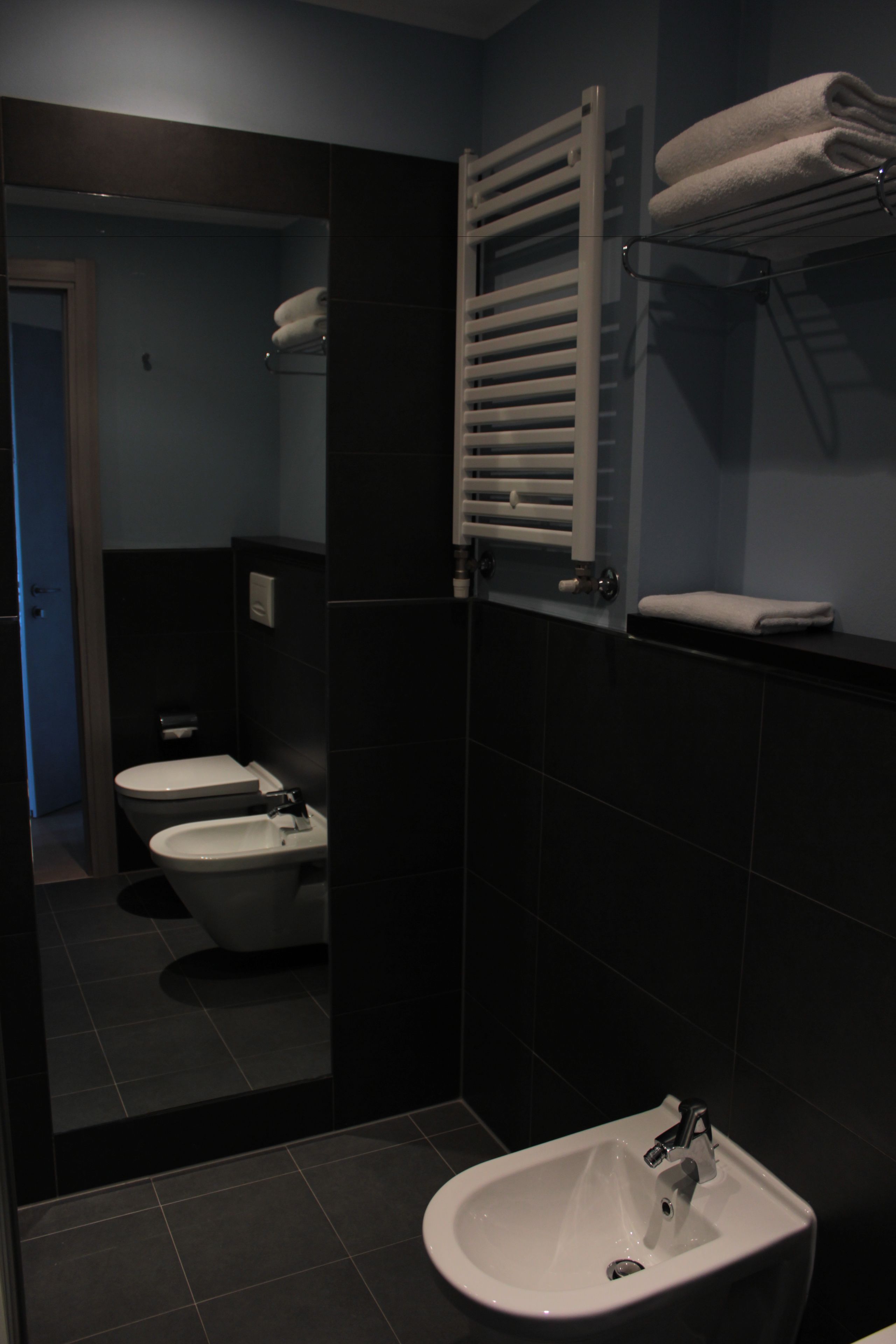 A modern bathroom with a white sink, two toilets, and a towel rack.