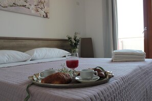 A neatly made bed with a tray of breakfast items including croissants, a glass of red juice, and a cup of coffee. - Mansio Residence Hotel (Elmas)