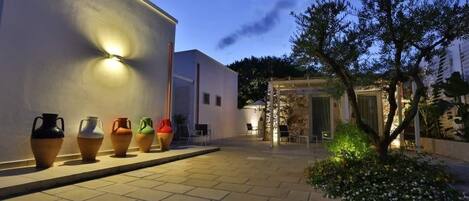 A courtyard with a row of colorful vases, a tree, and a building with a light fixture.
