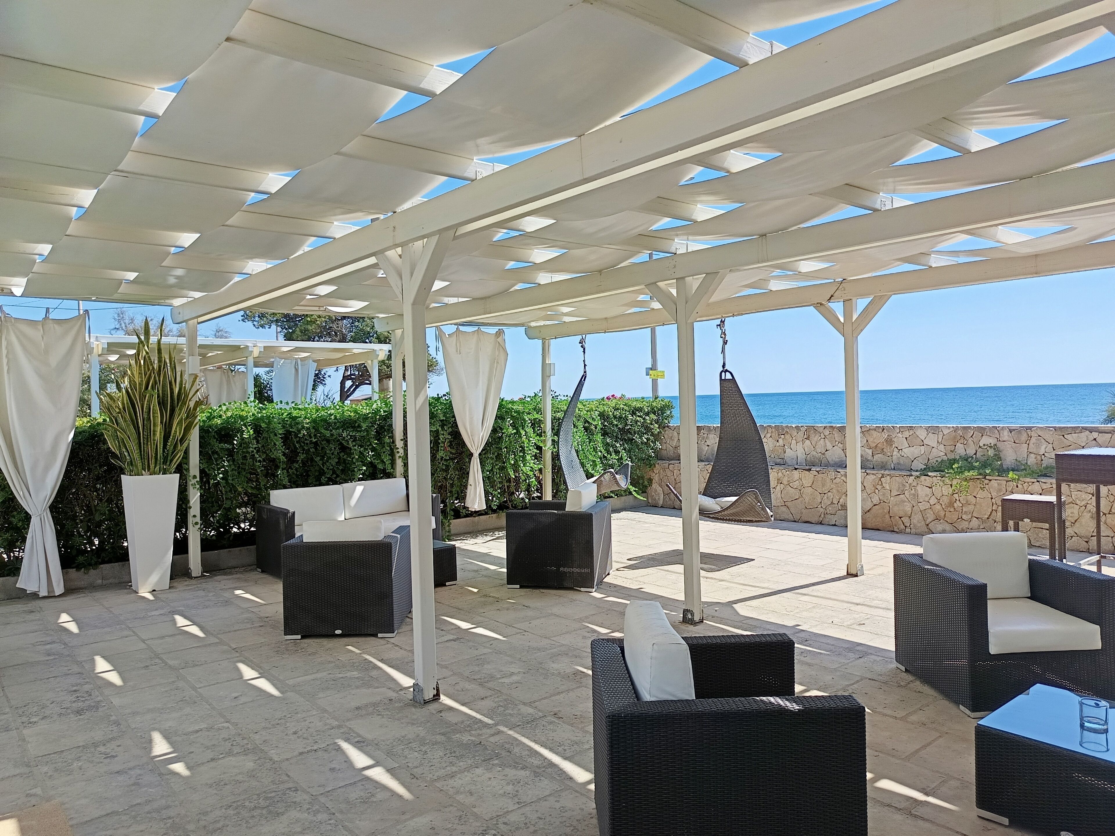 Un patio al aire libre con mobiliario de mimbre, plantas en macetas y vista al mar.