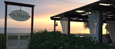 A resort entrance with a sign reading "la Siara Resort," a covered outdoor area, and a view of the sea at sunset.
