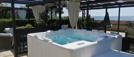A hot tub under a pergola with a view of the sea.