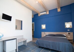 A bedroom with a bed, a desk, a chair, and a TV.