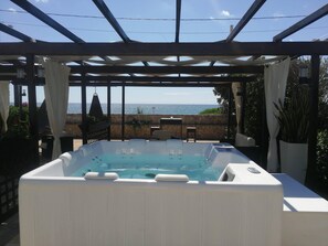 A hot tub under a pergola with a view of the sea.