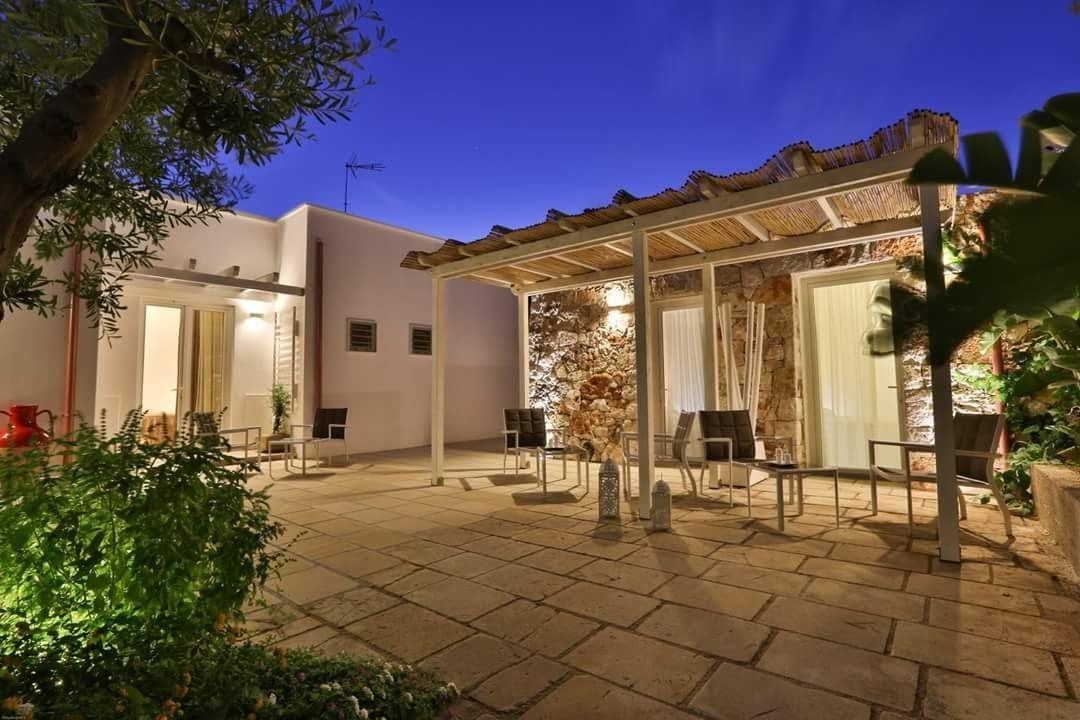 A courtyard with stone flooring, outdoor seating, and a covered area with a stone wall backdrop.