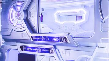 A futuristic room with a central control panel, a bed, and a seating area.