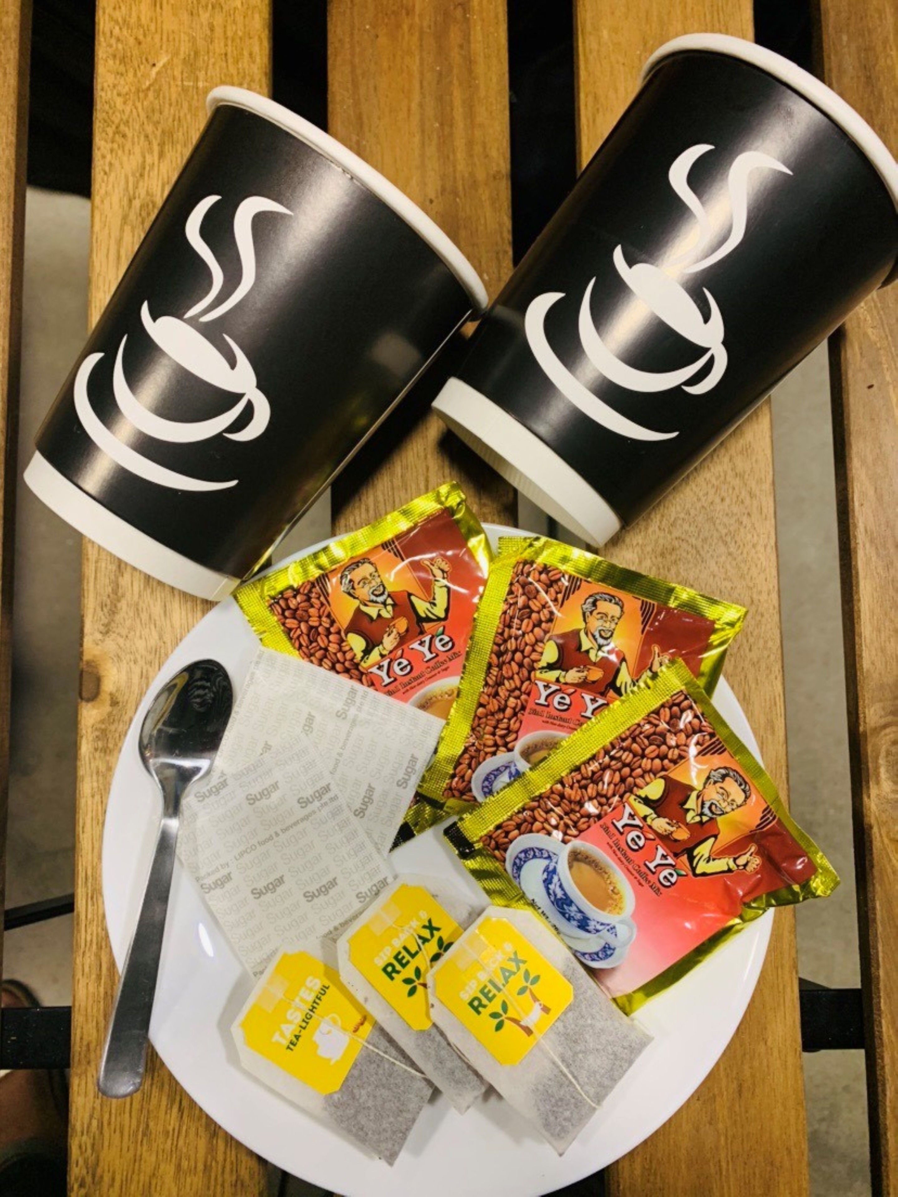 A plate with coffee cups, tea bags, and packets of instant coffee.