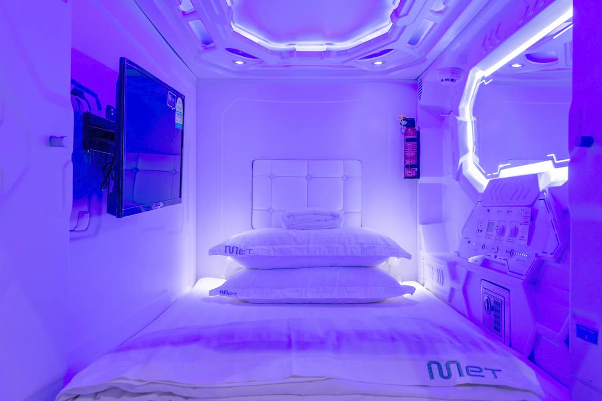 Quarto com cama, painel de controle e tela fixada na parede.
