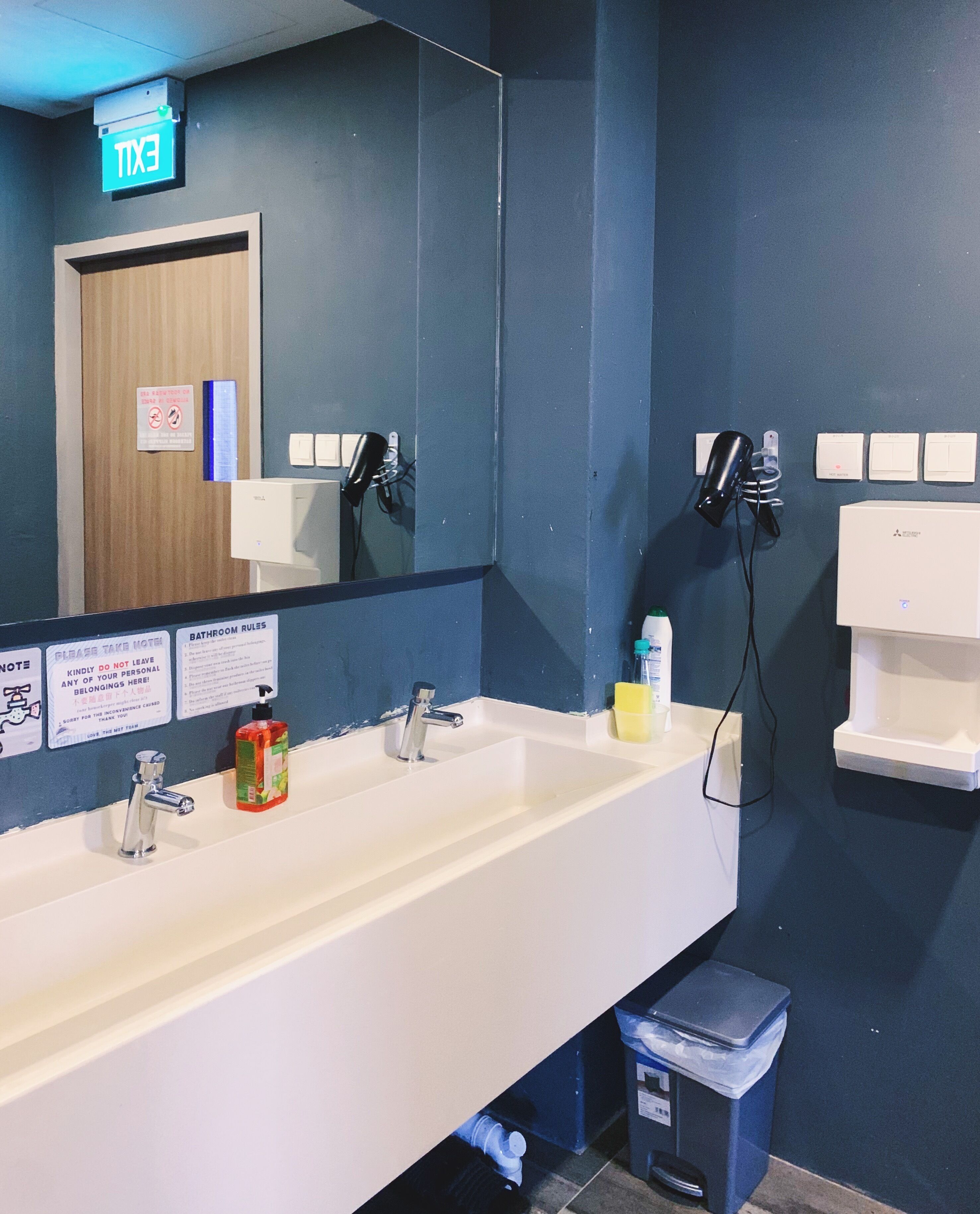 A bathroom with a white sink, two mirrors, a hairdryer, and a trash bin.