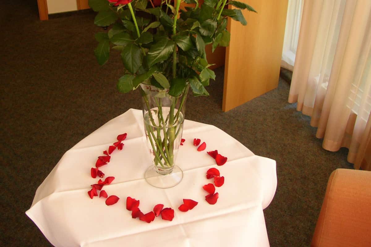 A table with a vase of red roses and rose petals arranged in a circle.