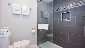 Un baño moderno con ducha de mampara de vidrio, inodoro y repisa con artículos de aseo.