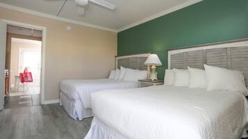 A hotel room with two beds, a ceiling fan, a nightstand with a lamp, and a view of the hallway.